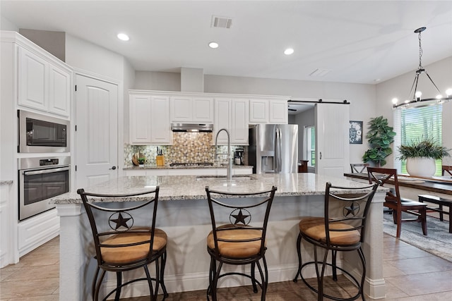 28026 Chuckwagon Trl, Magnolia, TX 77355 - kitchen with appliances with stainless steel finishes, a barn door, a sink, a center island with sink, and white cabinets