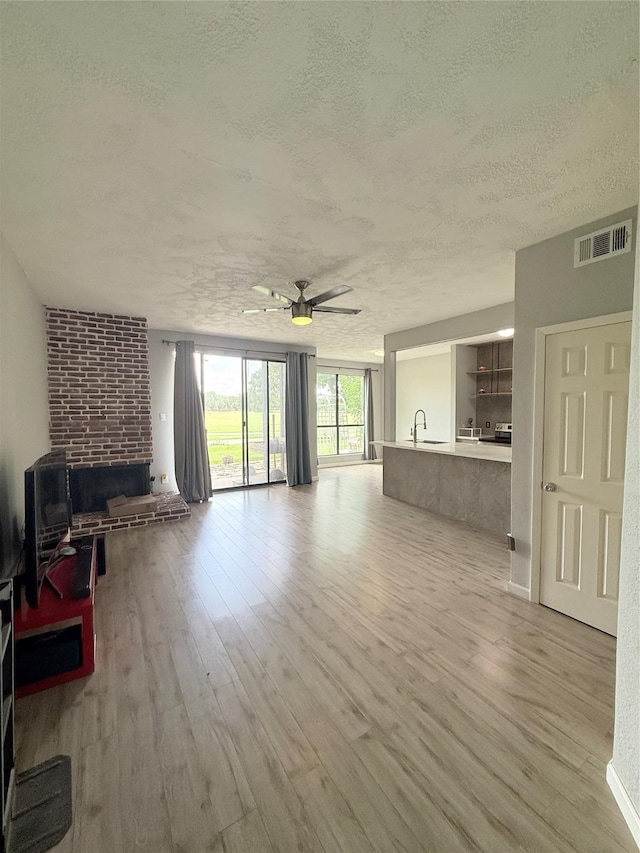 8149 Sands Point Dr Unit 113, Houston, TX 77036 - unfurnished living room featuring a textured ceiling, a ceiling fan, light wood finished floors, and a brick fireplace