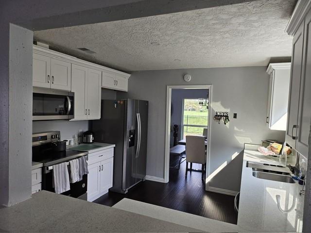 3311 Oyster Cove Dr, Missouri City, TX 77459 - kitchen featuring appliances with stainless steel finishes, dark wood-style floors, a sink, white cabinets, and a textured ceiling