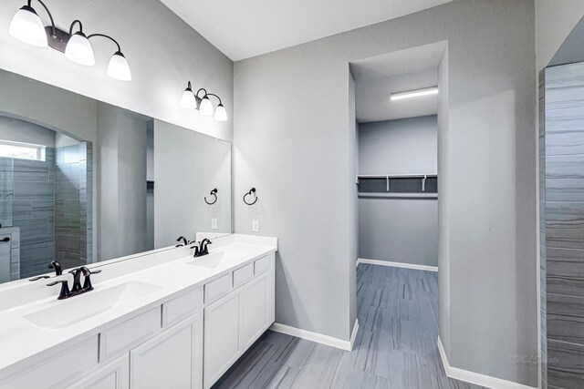 2410 Blazing Star Dr, Brookshire, TX 77423 - full bathroom featuring double vanity, baseboards, a spacious closet, tiled shower, and wood finished floors