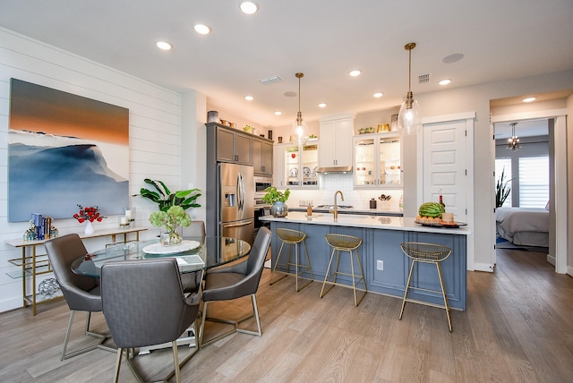 10914 Brambling Wood Dr S, Houston, TX 77043 - kitchen featuring stainless steel refrigerator with ice dispenser, light wood finished floors, a breakfast bar, decorative backsplash, and light countertops