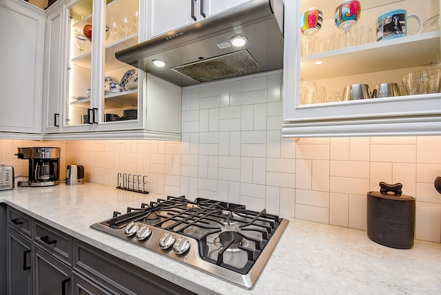 10914 Brambling Wood Dr S, Houston, TX 77043 - kitchen featuring stainless steel gas cooktop, under cabinet range hood, decorative backsplash, and glass insert cabinets