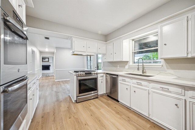 1802 Corral Dr, Houston, TX 77090 - kitchen featuring appliances with stainless steel finishes, a sink, white cabinets, and light wood-style floors