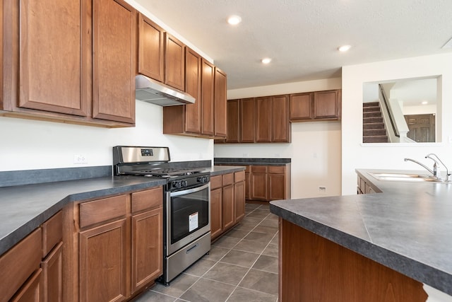 6120 Whitewing Rd, Rosenberg, TX 77469 - kitchen with stainless steel range with gas stovetop, a sink, under cabinet range hood, dark countertops, and dark tile patterned floors