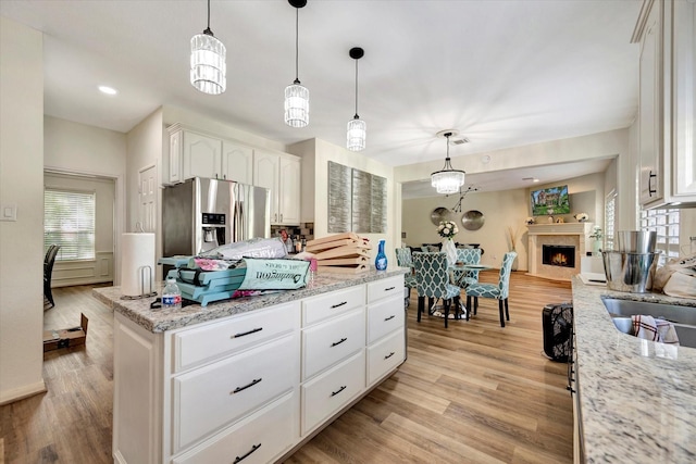 3602 Garrettsville Dr, Pearland, TX 77584 - kitchen featuring stainless steel fridge with ice dispenser, light wood-style floors, white cabinetry, and pendant lighting
