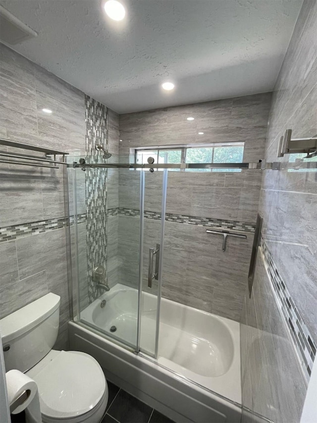 7802 Strathclyde Sound Rd, Houston, TX 77095 - bathroom featuring tile walls, bath / shower combo with glass door, toilet, a textured ceiling, and tile patterned floors