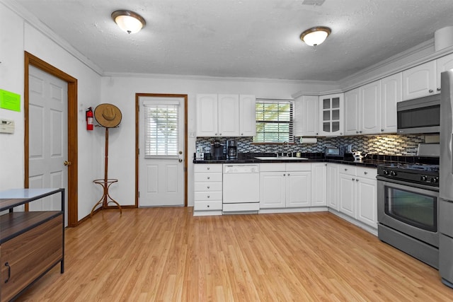 5614 Whipporwill Rd, Conroe, TX 77303 - kitchen featuring appliances with stainless steel finishes, light wood-style flooring, tasteful backsplash, white cabinetry, and crown molding