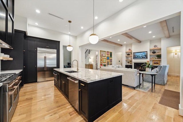 1917 Ebony Ln, Houston, TX 77018 - kitchen with premium appliances, dark cabinets, beamed ceiling, light wood-style floors, and a center island with sink