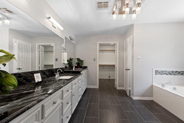 22402 Timber Ridge Dr, Magnolia, TX 77355 - bathroom featuring double vanity, baseboards, a garden tub, a spacious closet, and a chandelier