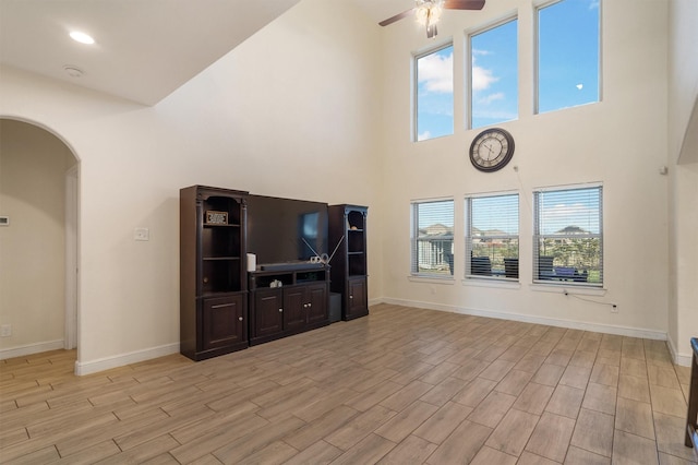 2715 Wembley Way, Rosenberg, TX 77471 - unfurnished living room with a ceiling fan, arched walkways, light wood-style floors, baseboards, and a towering ceiling