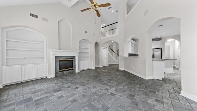 9710 Sotherloch Lake Dr, Spring, TX 77379 - unfurnished living room featuring built in features, ceiling fan, baseboards, a premium fireplace, and high vaulted ceiling