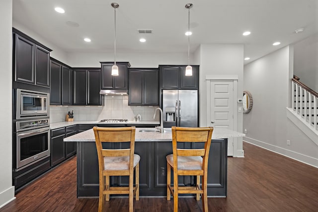 2027 Tarfite Pl, Houston, TX 77077 - kitchen featuring appliances with stainless steel finishes, a sink, under cabinet range hood, decorative backsplash, and a kitchen island with sink