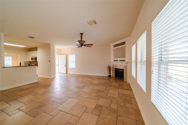 19422 Harvest Stream Way, Houston, TX 77084 - unfurnished living room with a tiled fireplace, a ceiling fan, baseboards, and light stone finish flooring