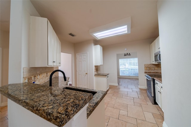 19422 Harvest Stream Way, Houston, TX 77084 - kitchen featuring stainless steel appliances, backsplash, stone tile floors, a peninsula, and white cabinets
