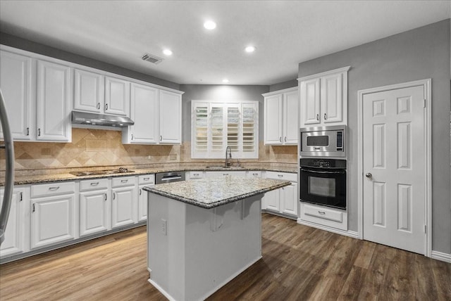 16610 Avenfield Rd, Tomball, TX 77377 - kitchen with black appliances, under cabinet range hood, white cabinets, wood finished floors, and recessed lighting