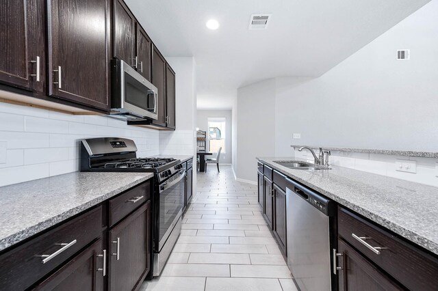 32322 Dusted Bronze Dr, Brookshire, TX 77423 - kitchen with stainless steel appliances, a sink, decorative backsplash, dark brown cabinets, and baseboards