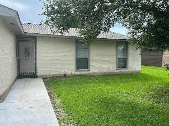 6322 Purple Sage Rd, Houston, TX 77049 - view of exterior entry featuring a yard, brick siding, and roof with shingles
