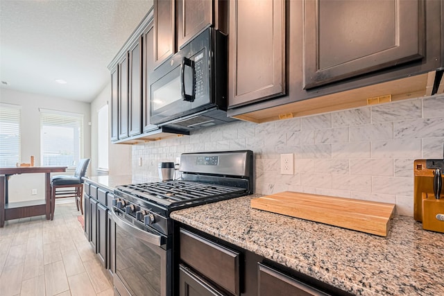 4507 Shallow Hill Ct, Houston, TX 77084 - kitchen featuring stainless steel gas stove, black microwave, backsplash, light stone counters, and dark brown cabinetry