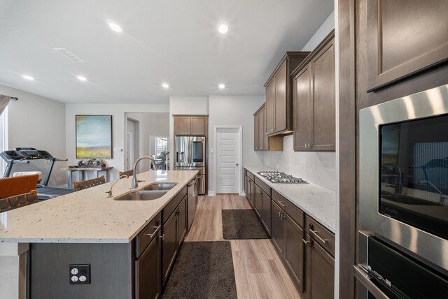 29023 Laurel Grove Ln, Fulshear, TX 77441 - kitchen featuring a sink, light wood finished floors, appliances with stainless steel finishes, an island with sink, and light stone counters