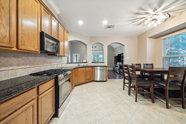 18411 S Raven Shore Dr, Cypress, TX 77433 - kitchen with appliances with stainless steel finishes, arched walkways, tasteful backsplash, brown cabinetry, and dark stone countertops