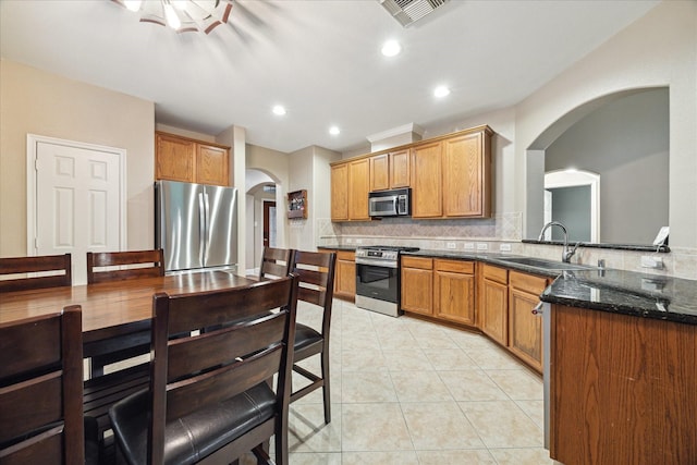 18411 S Raven Shore Dr, Cypress, TX 77433 - kitchen featuring appliances with stainless steel finishes, arched walkways, backsplash, light tile patterned floors, and dark stone counters