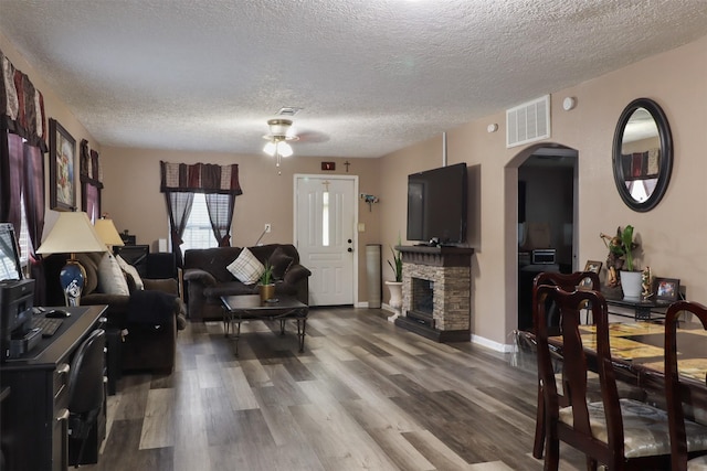 315 E Adoue St, Baytown, TX 77520 - living room featuring arched walkways, a textured ceiling, a ceiling fan, wood finished floors, and a stone fireplace