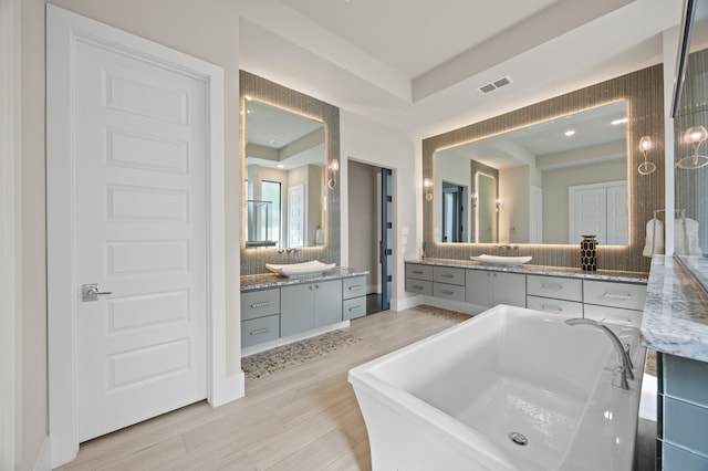 27927 Indigo Ridge Dr, Fulshear, TX 77441 - bathroom featuring a soaking tub, two vanities, wood finished floors, and tasteful backsplash