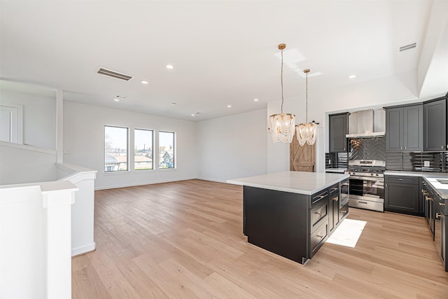 2320 Mills St, Houston, TX 77026 - kitchen with stainless steel range with gas cooktop, a center island, light countertops, a chandelier, and wall chimney range hood