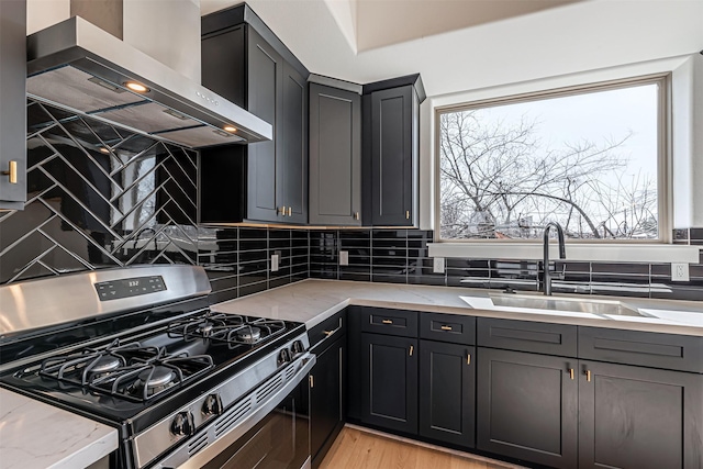 2320 Mills St, Houston, TX 77026 - kitchen with stainless steel range with gas stovetop, wall chimney range hood, a sink, light stone counters, and backsplash
