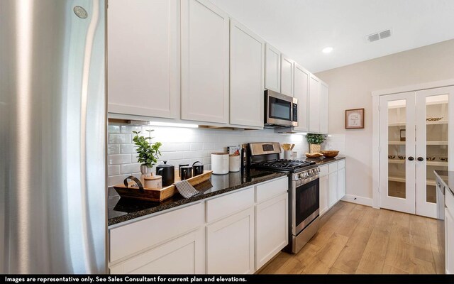 3644 Crosspointe Pass, Angleton, TX 77515 - kitchen with appliances with stainless steel finishes, decorative backsplash, white cabinetry, light wood finished floors, and dark stone countertops