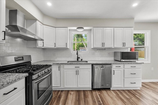 12153 24th St, Santa Fe, TX 77510 - kitchen with appliances with stainless steel finishes, a sink, wall chimney exhaust hood, light wood finished floors, and healthy amount of natural light