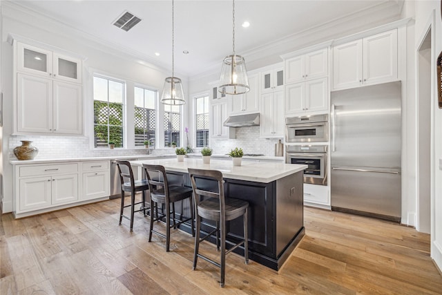7506 Little Caprese Ln, Houston, TX 77055 - kitchen with stainless steel appliances, under cabinet range hood, a kitchen island, white cabinetry, and crown molding