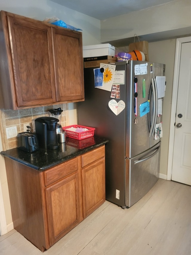 118 Whiting St, Galveston, TX 77550 - kitchen featuring freestanding refrigerator, brown cabinets, light wood-type flooring, backsplash, and dark stone counters