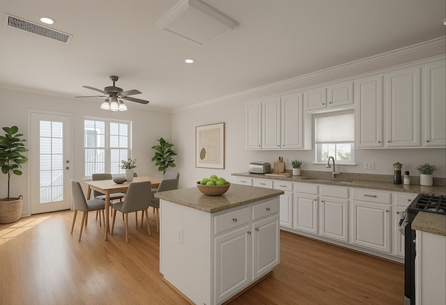 1108 W 22nd St, Houston, TX 77008 - kitchen featuring stainless steel range, a sink, crown molding, a center island, and white cabinetry