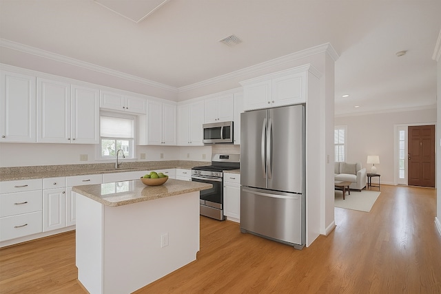 1108 W 22nd St, Houston, TX 77008 - kitchen featuring stainless steel appliances, a sink, white cabinets, ornamental molding, and light wood-style floors