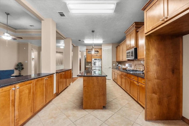 3707 Charleston St, Houston, TX 77021 - kitchen with appliances with stainless steel finishes, backsplash, brown cabinetry, light tile patterned floors, and decorative light fixtures