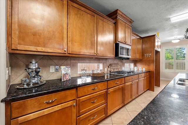 3707 Charleston St, Houston, TX 77021 - kitchen with stainless steel appliances, brown cabinets, dark stone countertops, backsplash, and light tile patterned floors