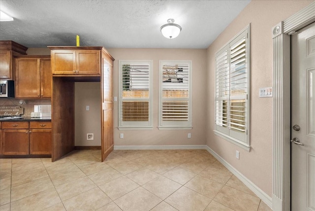 3707 Charleston St, Houston, TX 77021 - kitchen with brown cabinetry, stainless steel microwave, dark countertops, light tile patterned flooring, and a textured ceiling