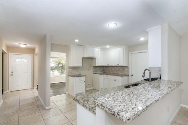 5807 Silver Forest Dr, Houston, TX 77092 - kitchen with a peninsula, light stone countertops, tasteful backsplash, white cabinetry, and light tile patterned floors