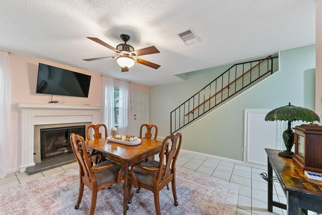 6506 Kentwick Dr, Houston, TX 77084 - dining space featuring light tile patterned floors, stairs, a ceiling fan, a fireplace with raised hearth, and a textured ceiling