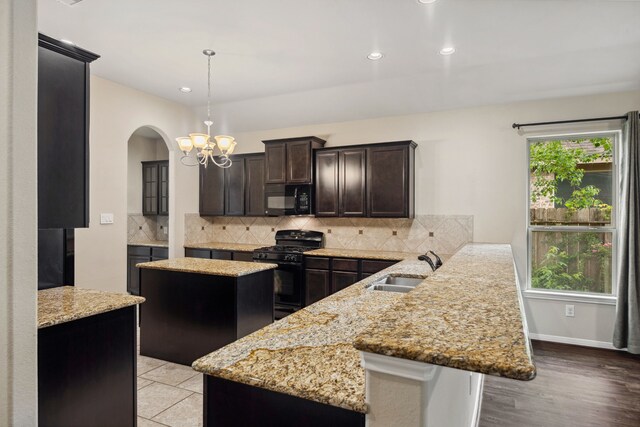 122 Jacobs Meadow Dr, Conroe, TX 77384 - kitchen featuring black appliances, a peninsula, arched walkways, a chandelier, and dark brown cabinetry