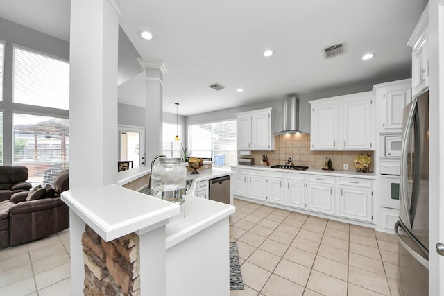 8742 Melting Shadows Ln, Houston, TX 77095 - kitchen with wall chimney exhaust hood, stainless steel appliances, ornate columns, light tile patterned flooring, and light countertops