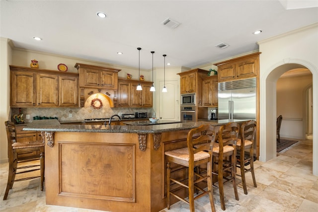 16119 Villa Fontana Way, Houston, TX 77068 - kitchen with built in appliances, brown cabinetry, arched walkways, a kitchen breakfast bar, and tasteful backsplash
