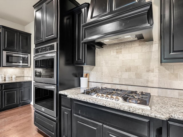 8322 Sands Bank Ln, Conroe, TX 77304 - kitchen featuring dark cabinetry, stainless steel appliances, extractor fan, decorative backsplash, and light stone countertops