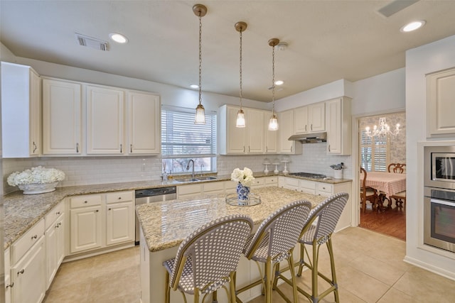 26 E Sterling Pond Cir, The Woodlands, TX 77382 - kitchen featuring a sink, appliances with stainless steel finishes, under cabinet range hood, a breakfast bar area, and light stone counters
