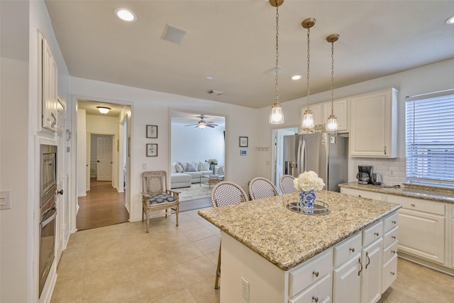 26 E Sterling Pond Cir, The Woodlands, TX 77382 - kitchen with stainless steel fridge, a center island, a breakfast bar area, recessed lighting, and light stone countertops