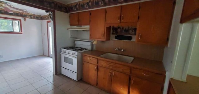 6136 25th St, Groves, TX 77619 - kitchen featuring gas range gas stove, a sink, under cabinet range hood, brown cabinetry, and light tile patterned floors