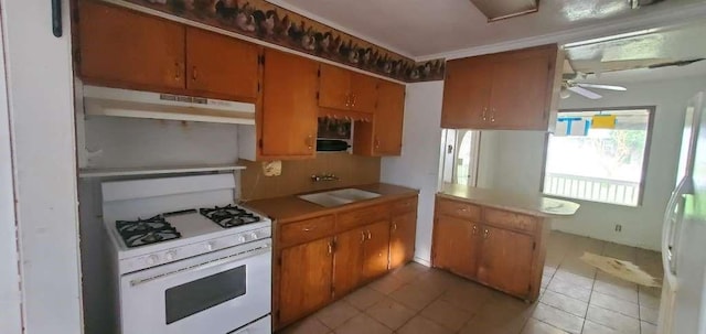 6136 25th St, Groves, TX 77619 - kitchen featuring white gas range, a sink, under cabinet range hood, light tile patterned floors, and brown cabinets