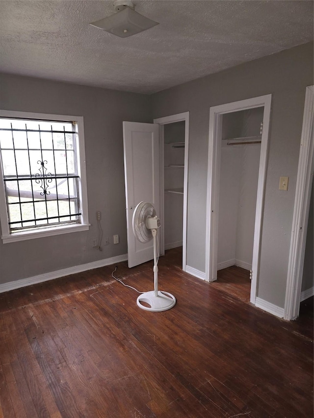 5318 Longmeadow St, Houston, TX 77033 - unfurnished bedroom featuring two closets, wood-type flooring, baseboards, and a textured ceiling
