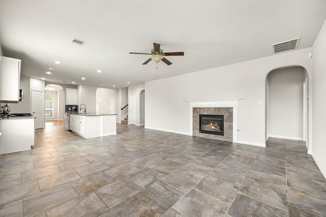 12510 Sherborne Castle Ct, Tomball, TX 77375 - unfurnished living room featuring ceiling fan, arched walkways, a tiled fireplace, a sink, and recessed lighting